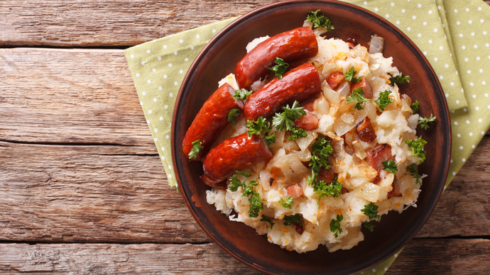A dish of warm Dutch stamppot topped with a chopped smoked sausage