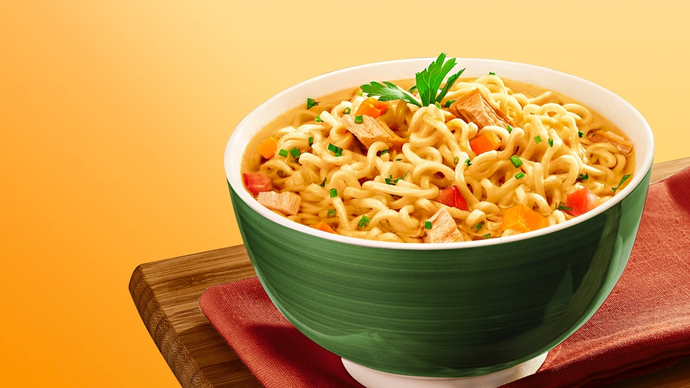 A green bowl containing loads of golden noodles mixed with veggies