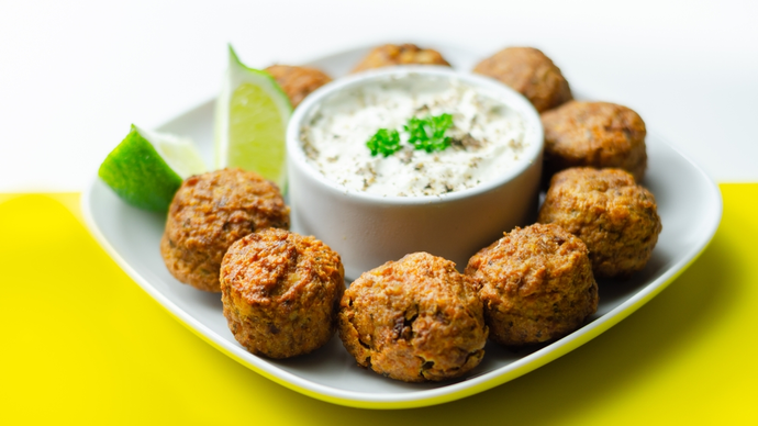 golden falafel pieces around a bowl of smooth cucumber and yogurt dip