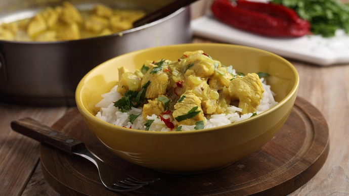 A bowl of turkey curry with rice on a table next to a larger serving bowl