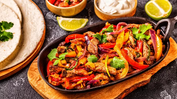 Crispy pork pieces in a pan with vegetable slices served alongside a plate of wraps