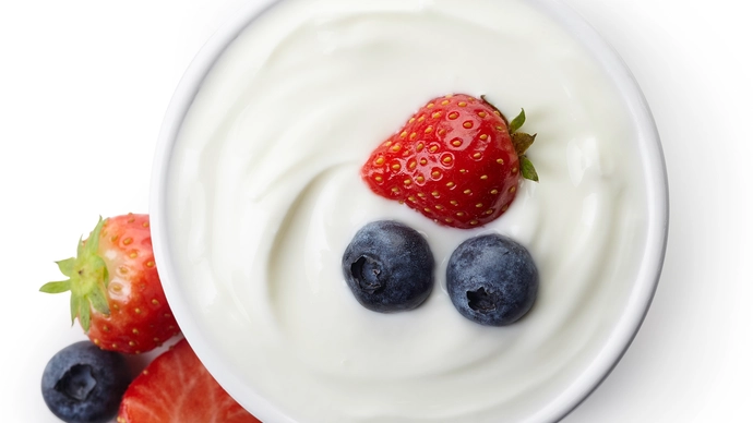 A bowl of yoghurt with a strawberry and a couple of blueberries on top