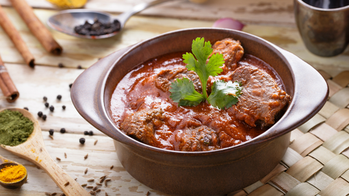 Powlen fach o rogan josh cig oen gyda garnais gwyrdd deiliog ar ei ben