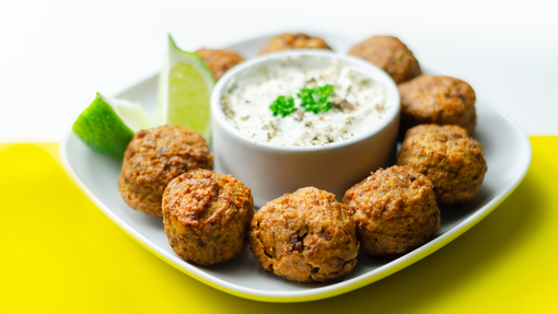 golden falafel pieces around a bowl of smooth cucumber and yogurt dip