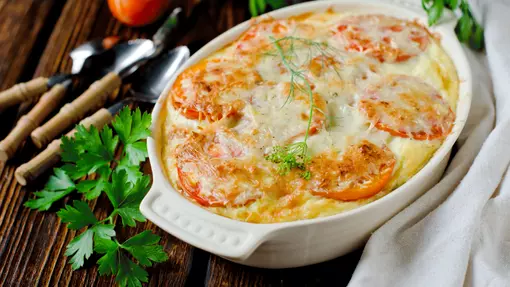 A traybake of golden turkey tomato gratin topped with whole tomato slices