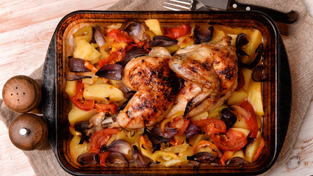 a traybake containing a crispy whole roast chicken surrounded by a variety of roasted bright vegetables