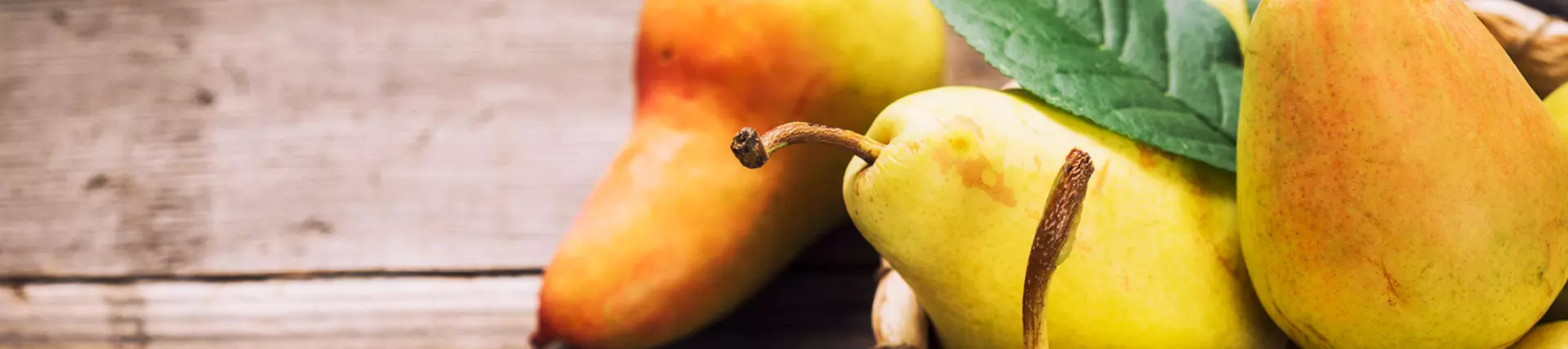 A photo of green and peach coloured pears spilling onto a dark wooden table top with green leaves scattered decoratively