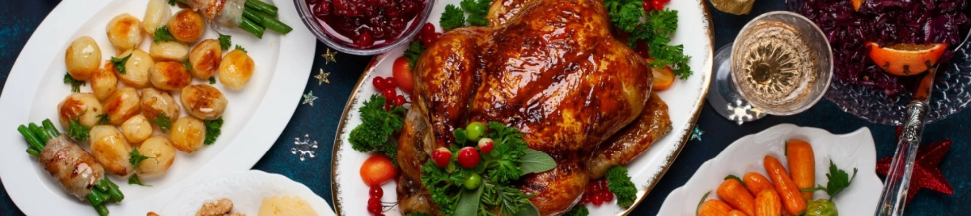 A birds eye view of a Christmas feast with a roast turkey in the centre, roasted root vegetables, a gravy boat and Christmas foliage spread around.