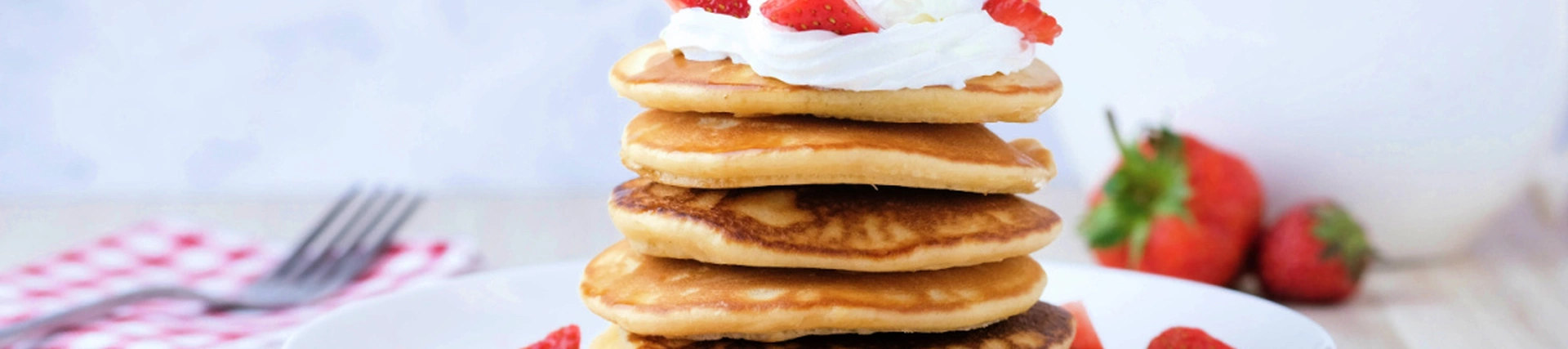 A stack of pancakes topped with strawberries and cream